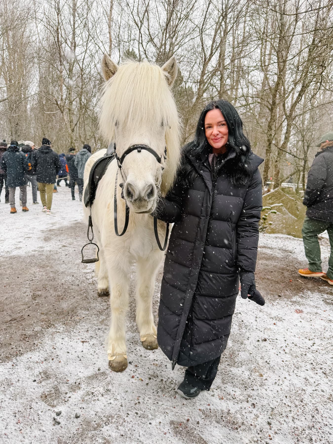 Nikki beside a white horse in light snow